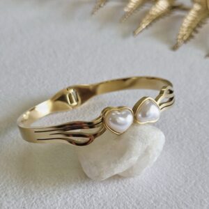 Gold-plated cuff bangle featuring twin white heart-shaped pearls.